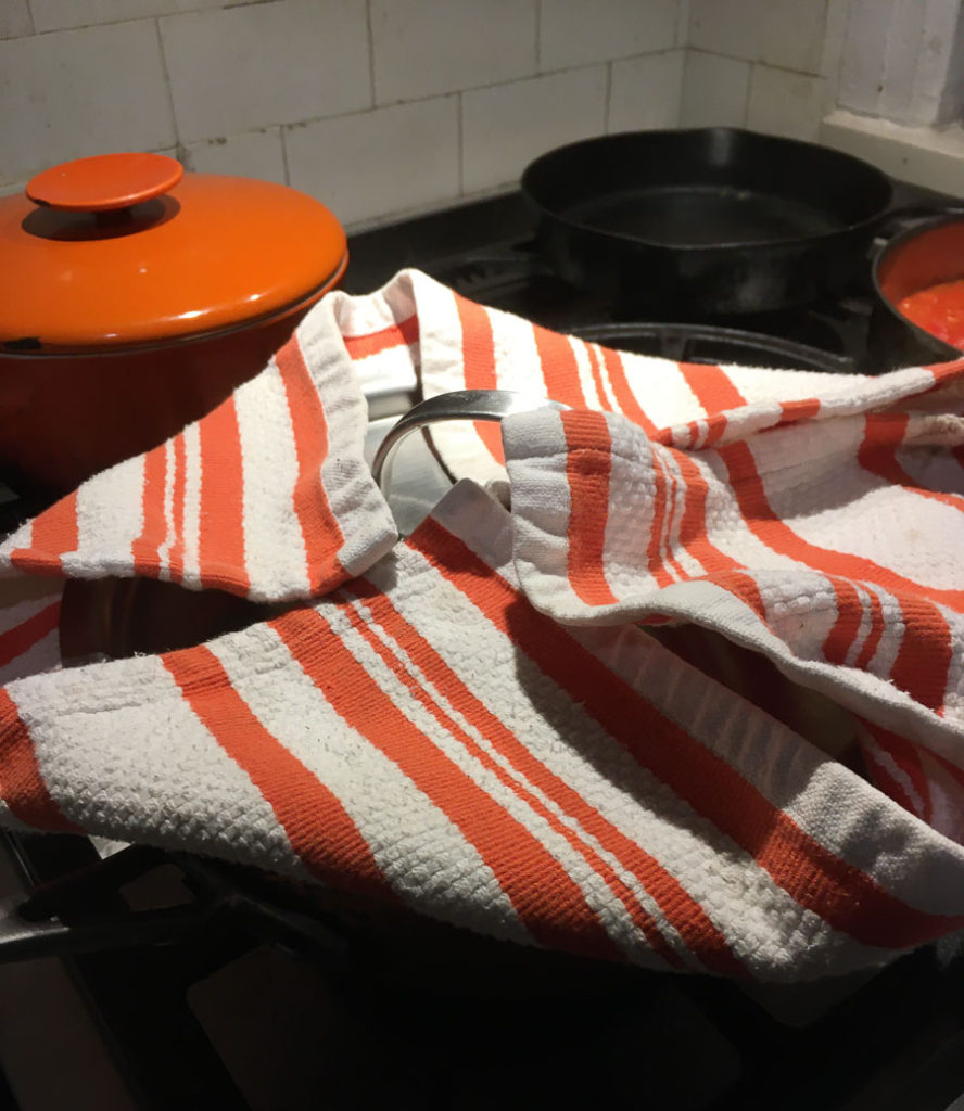 Orange-and-white striped tea towel on the top of a rice pot. The lid is placed on top of the towel and the corners of the towel are folded up over the lid.