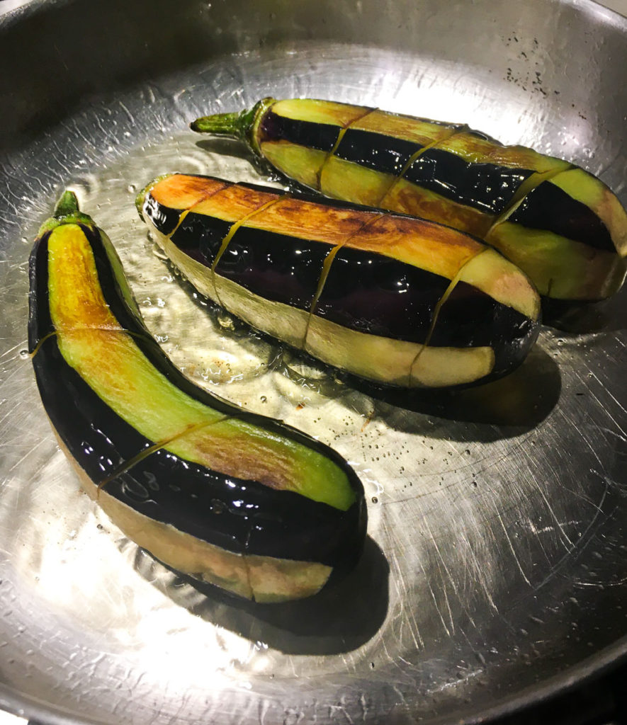 Thin eggplants peeled in long stripes, sizzling in olive oil in a stainless steel pan