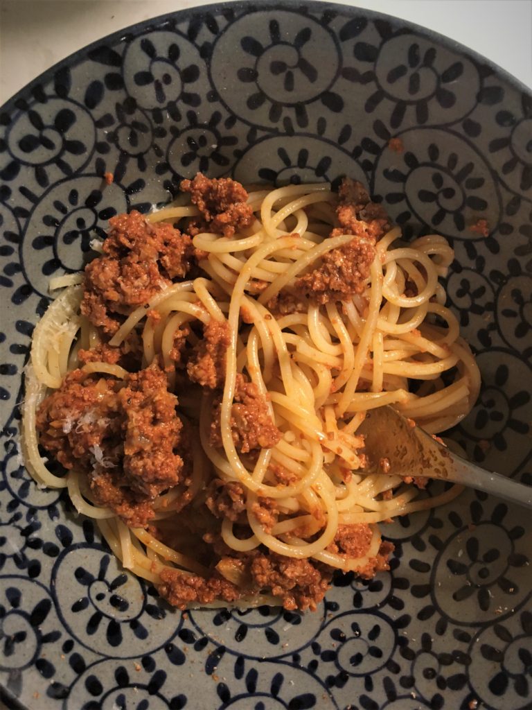 Meat sauce on spaghetti in a blue and gray bowl.