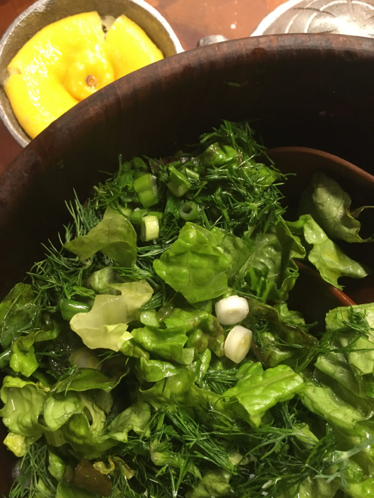 Lettuce salad in a wooden bowl, with a lemon on the side.