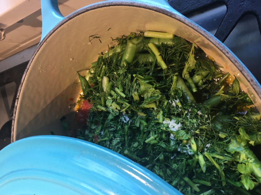 Fresh ingredients for Greek-style green beans layered in the pot, before cooking: beans, tomato, herbs, salt.